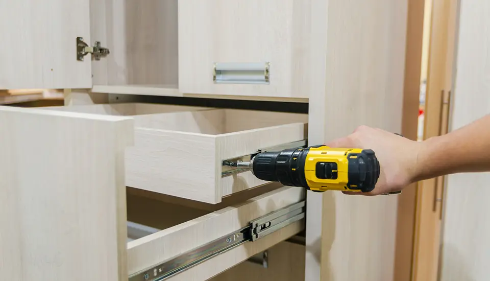 Montage einer Schublade in einem hellen Holzschrank mit Akkuschrauber.